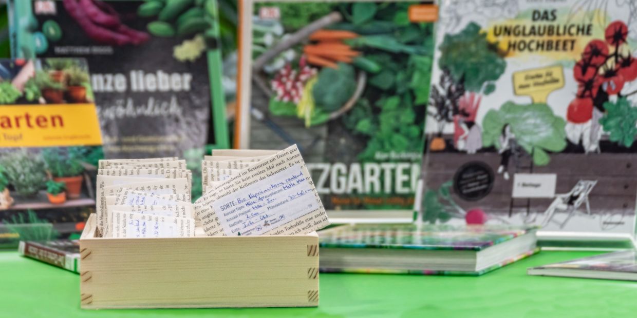 Stadtbibliothek Linz Papiersackerl mit Saatgut und Bücher im Hintergrund