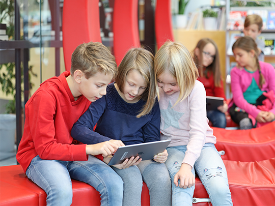Drei Kinder sehen sich gemeinsam etwas auf einem Tablet an